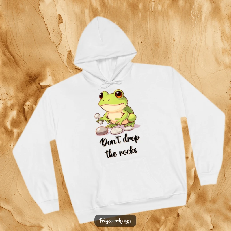 Funny hoodie with a determined kawaii frog focused on juggling three shiny pebbles, representing dedication and humorous perseverance.